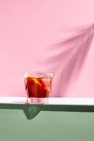 Negroni cocktail over pink background. Drink in rox glass in daylight with palm leaf hard shadow. Summer, tropical, fresh drink concept.の写真素材