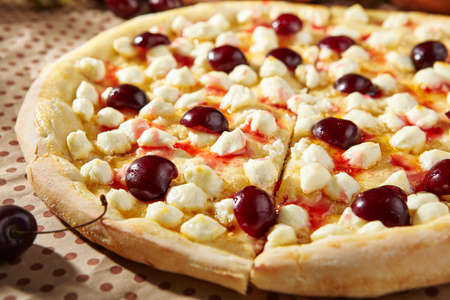 Cherry Cheese Pizza - homemade dessert pizza is made with a buttery dough, cherry and cream cheese. Sweet pizza on paper with ripe sweet cherry and wooden plate. Dessert lunch in rustic styleの写真素材