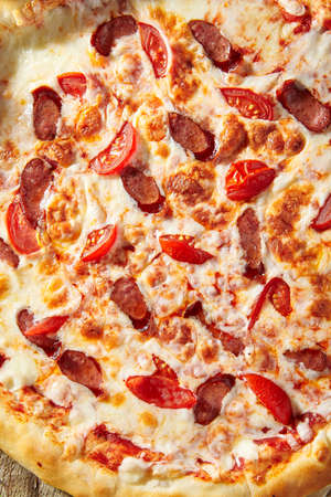 Spicy Sausage Italian Pizza with tomato, mozzarella cheese, sausage slice. Homemade pizza on baking paper with food ingredients on wooden table. Fast food or junk food pizza dinner top viewの写真素材