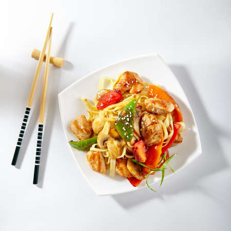 Udon noodles with sweet and sour chicken and vegetable. Asian style noodles food on white background. Udon in white plate with wooden choopsticks. Top viewの写真素材