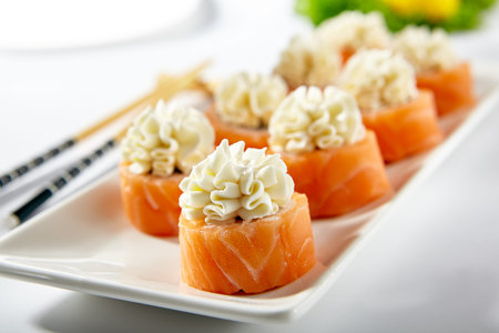 Philadelphia Sushi Roll made with Smoked Salmon. Maki sushi topped with cream cheese. White plate with wooden chopstick on white tableの写真素材