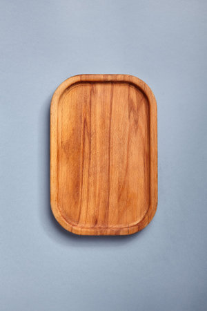 Empty wooden tray on textured dark blue table. Rectangular wooden dish top view. Kitchen minimal...