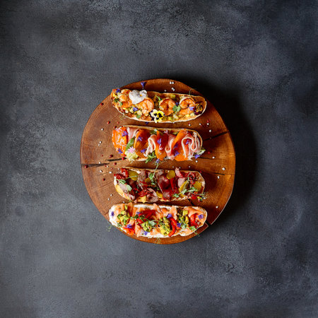 Italian Bruschetta antipasto - Grilled Bread topped with tomato, vegetables, cured meat, salted fish. Various bruschetta on dark textured table top view. Food flat lay, italian rustic dish conceptの写真素材