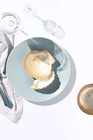 Oyster shell on blue dish. Crystal white tablecloth with glass of water, gray napkin, fork and knife. Minimal seafood cafe table top view. Summer day concept with white table top viewの写真素材