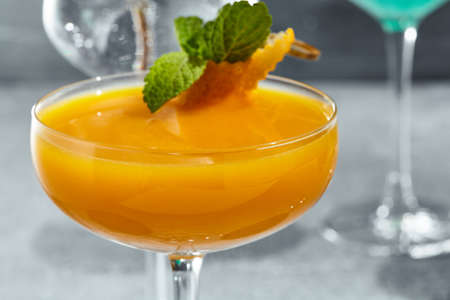 Cocktail with vodka and mango. Summer day cocktail concept with sunlight and shadow. Cocktail garnished with mint leaf and orange peelの写真素材