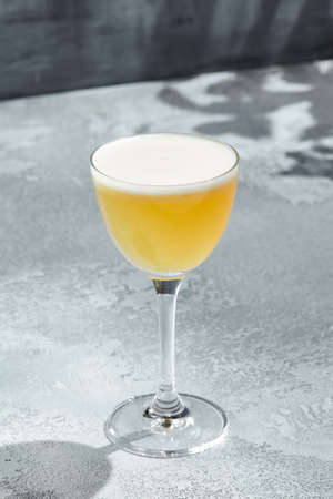 Whisky Sour Cocktail is a whiskey based cocktail with egg white. Vintage table with sunshine and shadow. Strong alcohol drink with whisky, sugar syrup and lemon juiceの写真素材