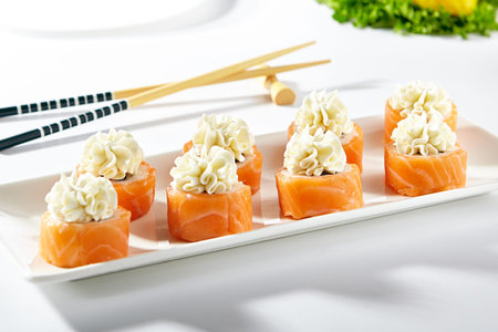Philadelphia Sushi Roll made with Smoked Salmon. Maki sushi topped with cream cheese. White plate with wooden chopstick on white tableの写真素材