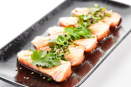 Salmon tataki - seared salmon, thinly sliced sashimi style. Salmon tataki served with delicious citrus ponzu tataki sauce and fresh greens. Japanese seafood on black plate isolated on white backgroundの写真素材