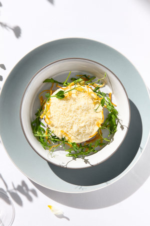 Beef tartare under cheese sauce with deep fried onion. Fancy dinning with beef tartare on white table with simple contemporary decoration. Sunlight and harsh shadow still life. Beef tartare blue dishの写真素材