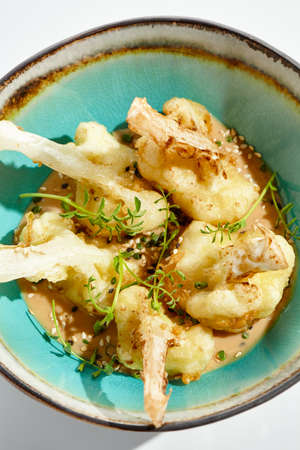 Fried tempura cauliflower with peanut sauce in bowl. Vegetarian hot dish - florets cabbages roasted in batter on white background. Veggie menu for asian restaurant. Hot vegan appetizers plant basedの写真素材