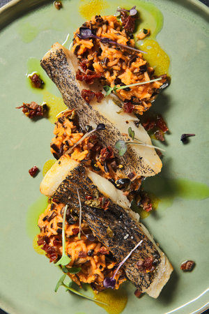 Risotto with slice roasted white fish in green plate on black background. Grilled code with mix...
