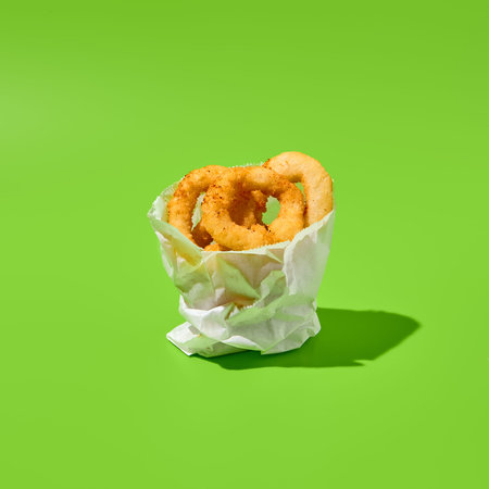 Fried onion rings in paper bag on green background. Flying onion rings in minimal style. Fast food...
