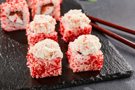 Maki sushi on dark slate. Maki roll with crab topped. Sushi roll with crab, cream cheese and tobika. Style concept japanese menu with black background, leaves and hard shadowの写真素材