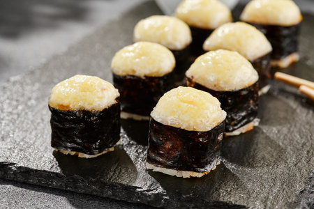 Baked Maki sushi on dark slate. Hot cheese hosomaki roll. Simple sushi roll with cheese, baked cheese topped. Style concept japanese menu with black background, leaves and hard shadowの写真素材