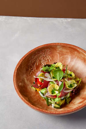 Salad with pastrami, vegetables and dressing on handmade ceramic bowl. Vegetables salad with roast beef in modern dishware on gray stone background. Contemporary food from chef. handmade dinner plateの写真素材