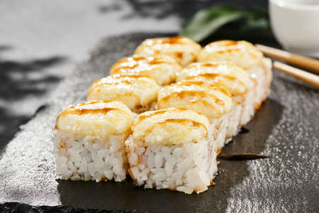 Baked Maki sushi on dark slate. Hot cheese maki with unagi sauce. Sushi roll with baked cheese and unagi sauce topped. Style concept japanese menu with black background, leaves and hard shadowの写真素材