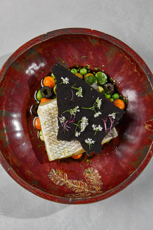 Cooked white fish steak on vegetable balls. Fish fillet with vegetables garnish in handmade ceramic...