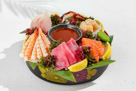 Sashimi set from raw seafood: salmon, tuna, eel, perch, shrimps, sea scallop. Traditional japanese dish - sashimi on white background. Fresh delicacy on ice with lemon, ginger and sauceの写真素材