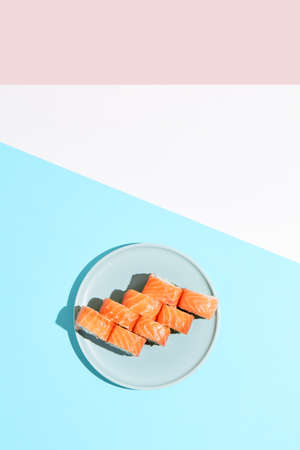 Classic sushi roll with salmon outside, crab, cheese and cucumber inside. Philadelphia maki in minimal style. Modern japanese menu concept. Salmon maki roll on ceramic plate on colored backgroundの写真素材