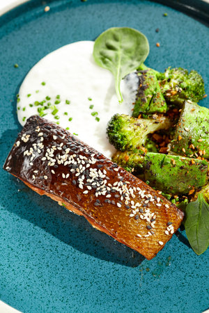 Roast salmon with crispy skin, grilled vegetables and espuma. Grilled salmon fillet with broccoli, avocado and white sauce. Keto food - baked fish with skin and green vegetables on white backgroundの写真素材