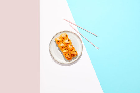 Hot maki roll with cheese on colored background. Baked sushi roll with salmon inside, rice outside, cheese topped. Maki sushi in minimal style. Japanese menu conceptの写真素材