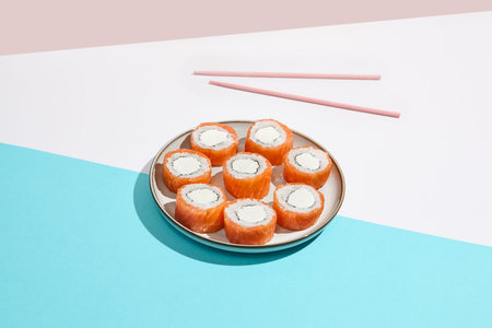 Philadelphia maki roll on ceramic plate with chopsticks. Salmon sushi roll with philadelphia cheese...