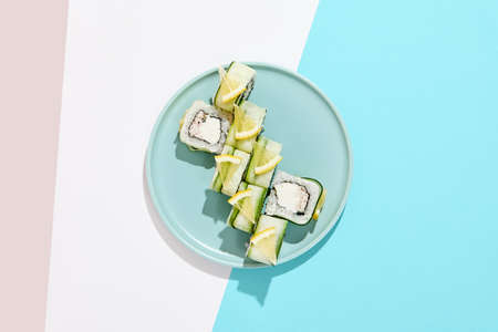Fresh maki roll with crab on colored background. Sushi roll with crab and cheese inside, cucumber and lemon outside. Green Maki sushi in minimal style. Japanese menu conceptの写真素材