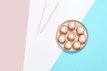 Philadelphia maki roll on ceramic plate with chopsticks. Salmon sushi roll with philadelphia cheese on colored background. Japanese menu concept. Salmon sushi roll modern styleの写真素材