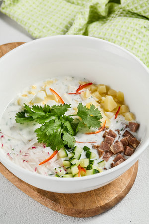 Traditional russian soups - okroshka with fresh vegetables, meat and kefir. Cold summer soup on white table. Aesthetic composition with traditional russian food and spices, textile.の写真素材