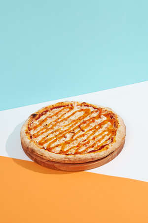 Italian pizza with chicken and sweet sour sauce on colored background. Chicken pizza with creamy sauce and cheese in minimal style on blue color. American pizza delivery concept with color backdropの写真素材