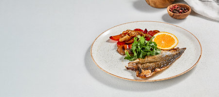 Fish dish - roasted dorado fillet with vegetables. Grilled fish fillet and roasted paprika, tomatoes and onion. Roast dorado fillet with garnish, greens and lemon on ceramic plateの写真素材