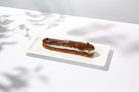 Chocolate eclair on white plate. French dessert stuffed custard cream. Eclair with coffee flavours....