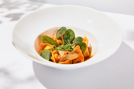 Tradition italian stuffed pasta - tortellini with minced meat. Italian ravioli on white background with harsh shadows. Summer menu italian restaurant. Tortellini with beef and spinach leaves.の写真素材