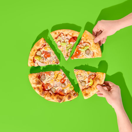 Sliced thick-crust pizza with ham, mushrooms, olives on a bright green background. Two hands grabbing pieces. Minimalist style, top view.の写真素材