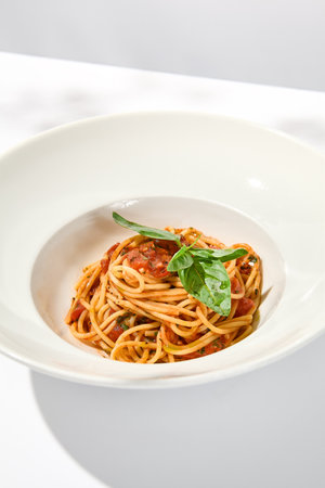 Vegetarian pasta with basil and tomatoes on white plate. Tomato pasta in summer menu with hard shadows. Spaghetti with tomatoes on light background. Vegan food - spaghetti marinaraの写真素材