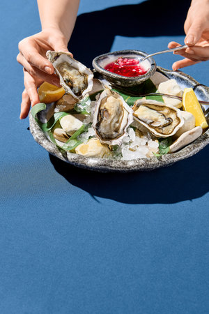 Vertical side view of a woman's hand picking up a fresh oyster, a luxury dining moment capturedの写真素材