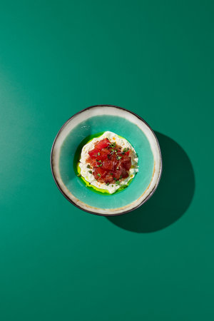 Top view of tuna tartare with stracciatella, served in a ceramic bowl. Asian restaurant setting with stark shadows, monochrome green, and minimalist design.の写真素材