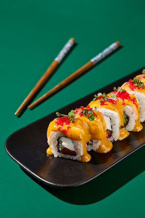 Closeup of maki sushi with salmon, curry sauce, and tobiko roe on black plates against a deep green, monochrome background.の写真素材