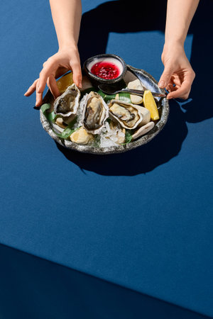 Vertical side view of a woman's hand picking up a fresh oyster, a luxury dining moment captured
