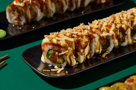 Detailed closeup of a sushi set on black plates, contrasting against a bold green background. Shadows and chopsticks add intrigue to this Asian restaurant menu image.の写真素材