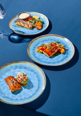 A set of Asian-style dishes featuring salmon, cod, and pike perch, presented on blue ceramic plates...