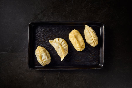 Modern-style Uzbek manty served on a black plate over a black marble table, showcasing Uzbek culinary tradition.の写真素材