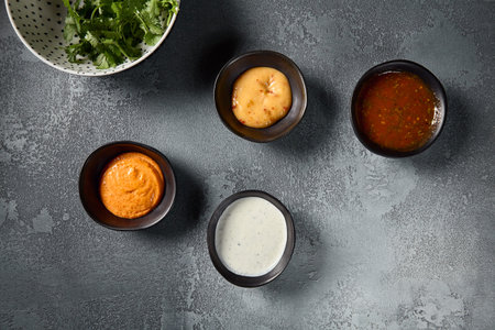 A top view shot displaying a variety of sauces in individual bowls, gracefully laid out on a gray...