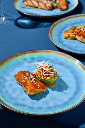 Close-up vertical shot of grilled cod in unagi sauce with vegetables and avocado on a ceramic plate,...