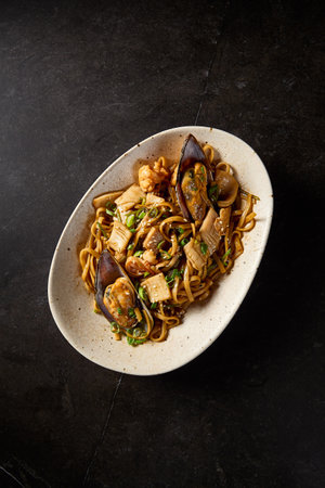 Vertical top perspective of udon pasta teeming with delectable seafood, showcased on a ceramic dish with an Asian flair, poised on a black canvas.の写真素材