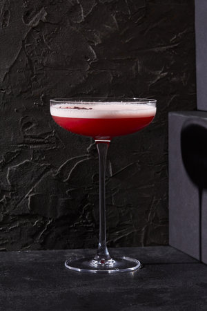 Berry-infused sour cocktail with hibiscus tea, elegantly poured into a stemmed glass, standing out against a stark black setting with sharp shadows.の写真素材