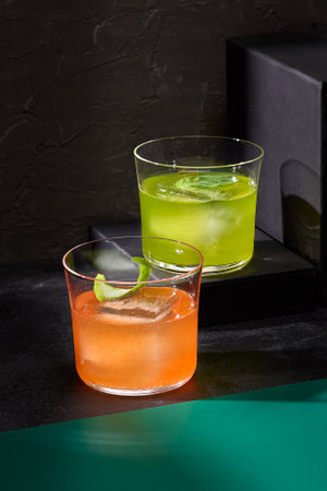Gin tonics elegantly infused with basil and bergamot, casting stark shadows on a black backdrop, defining minimalist bar artistry.の写真素材
