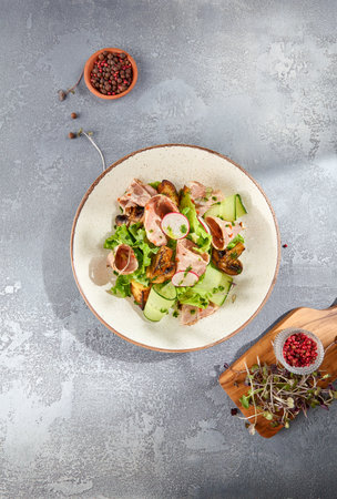 Vertical top-view of a delicious salad with baked meat and vegetables, served on a ceramic plate. Gray concrete background with ample copy space.の写真素材