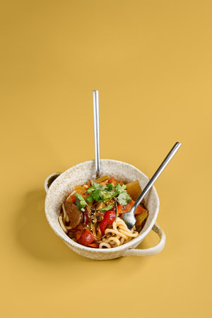 A rustic artisan bowl of Lagman soup with two utensils stands ready to enjoy, showcasing a symphony of noodles, beef, vegetables, and herbs.の写真素材