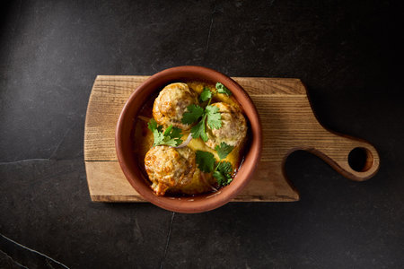 Horizontal top view of baked mushrooms filled with lamb mince and cilantro, elegantly presented on a Georgian clay plate 'keci', set against a dark backdrop on a wooden board.の写真素材